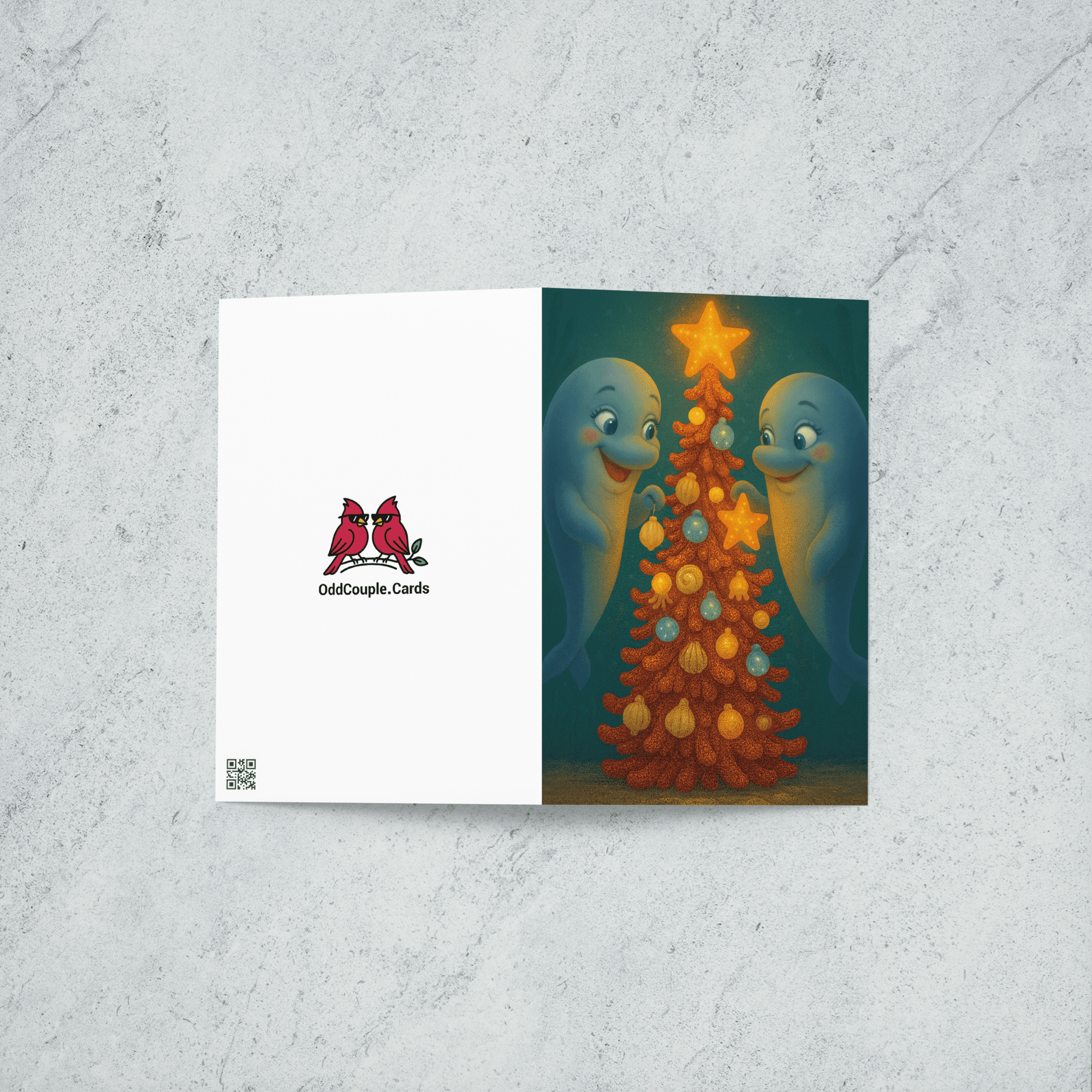A Christmas card featuring two dolphins decorating an underwater tree with shells, ornaments, and a large starfish. Back of card features the OddCouple.Cards logo.